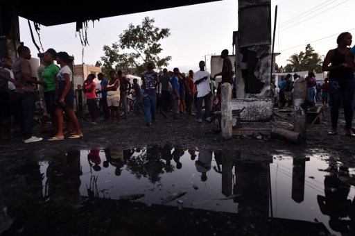 Haitians look at the damage caused by a fire after an explosion at a gas station in Hinche, 110 km from Port-au-Prince. At least seven people were burned and about thirty others seriously injured Thursday in Haiti by the explosion of a tanker carrying fuel for the oil company Total, according to the Haitian Civil Protection. / AFP / HECTOR RETAMAL
